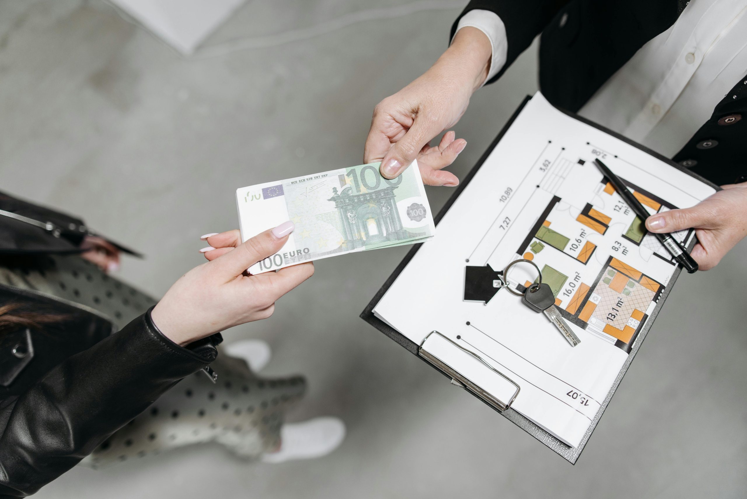Close-up of a real estate transaction with euro bill, keys, and floor plan.